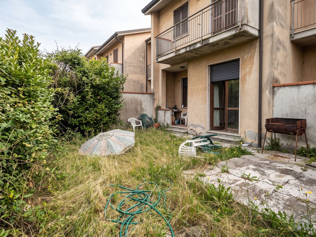Prima: giardino trascurato con erba alta, ombrellone rovesciato e sedie di plastica.