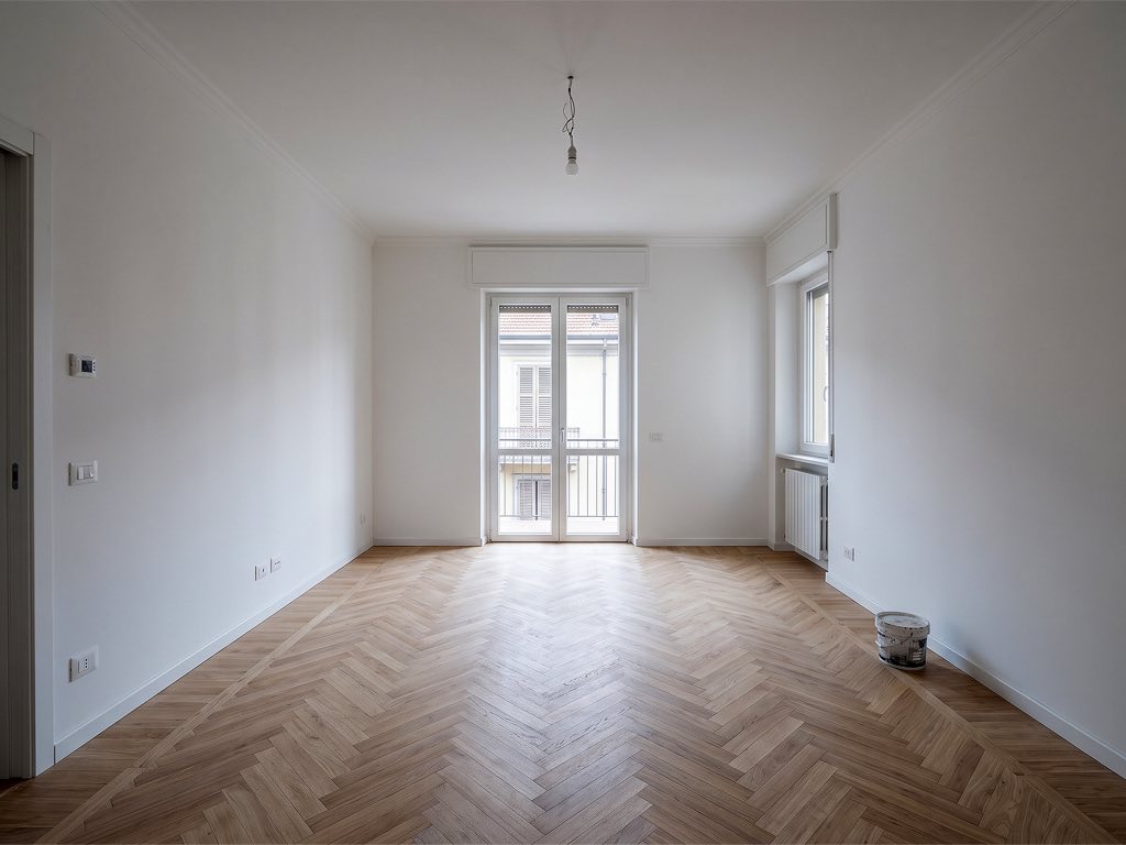 Prima: soggiorno ristrutturato completamente vuoto con parquet a spina di pesce.